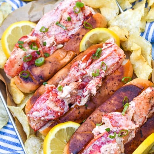 three homemade lobster rolls on a metal serving pan with potato chips on the sides