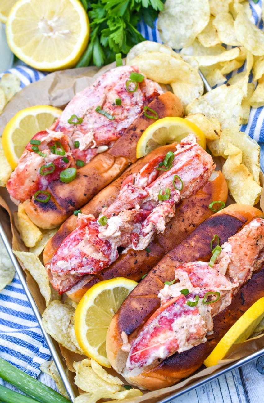 three homemade lobster rolls on a metal serving pan with potato chips on the sides