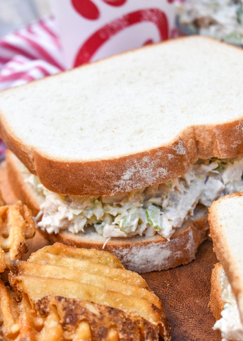 chick fil a's chicken salad between two slices of white bread on a wooden cutting board