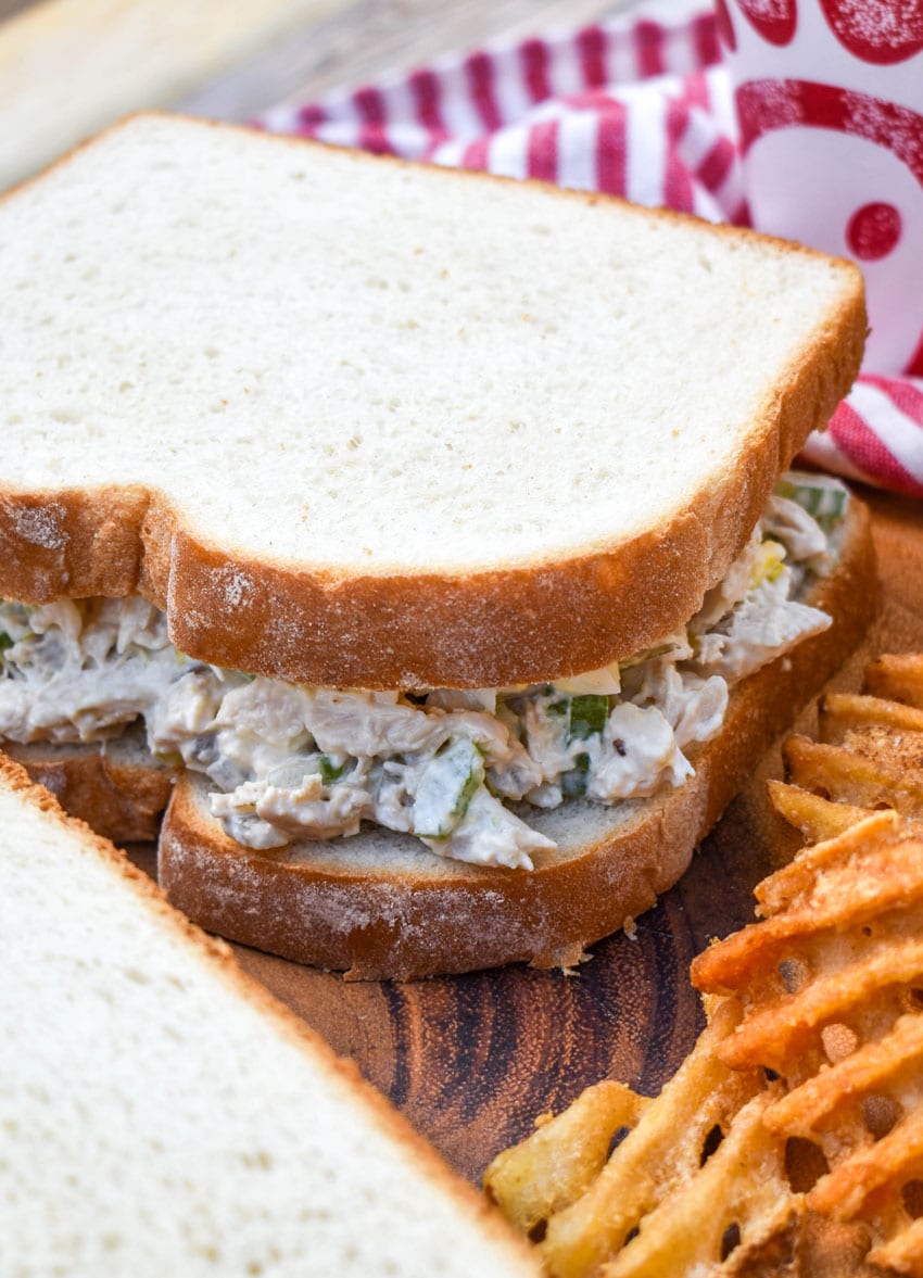 chick fil a's chicken salad between two slices of white bread on a wooden cutting board
