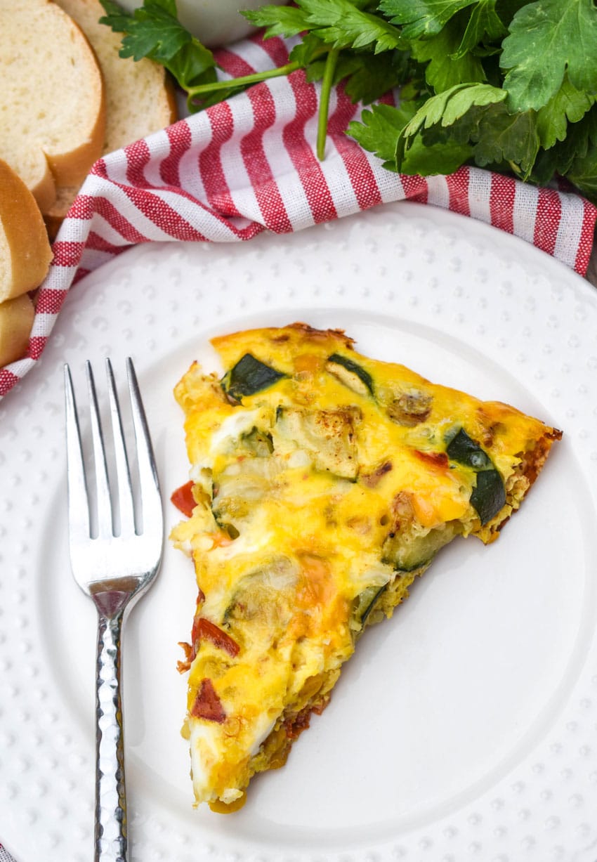 a slice of garden vegetable fritatta on a small white plate with a silver fork resting on the side