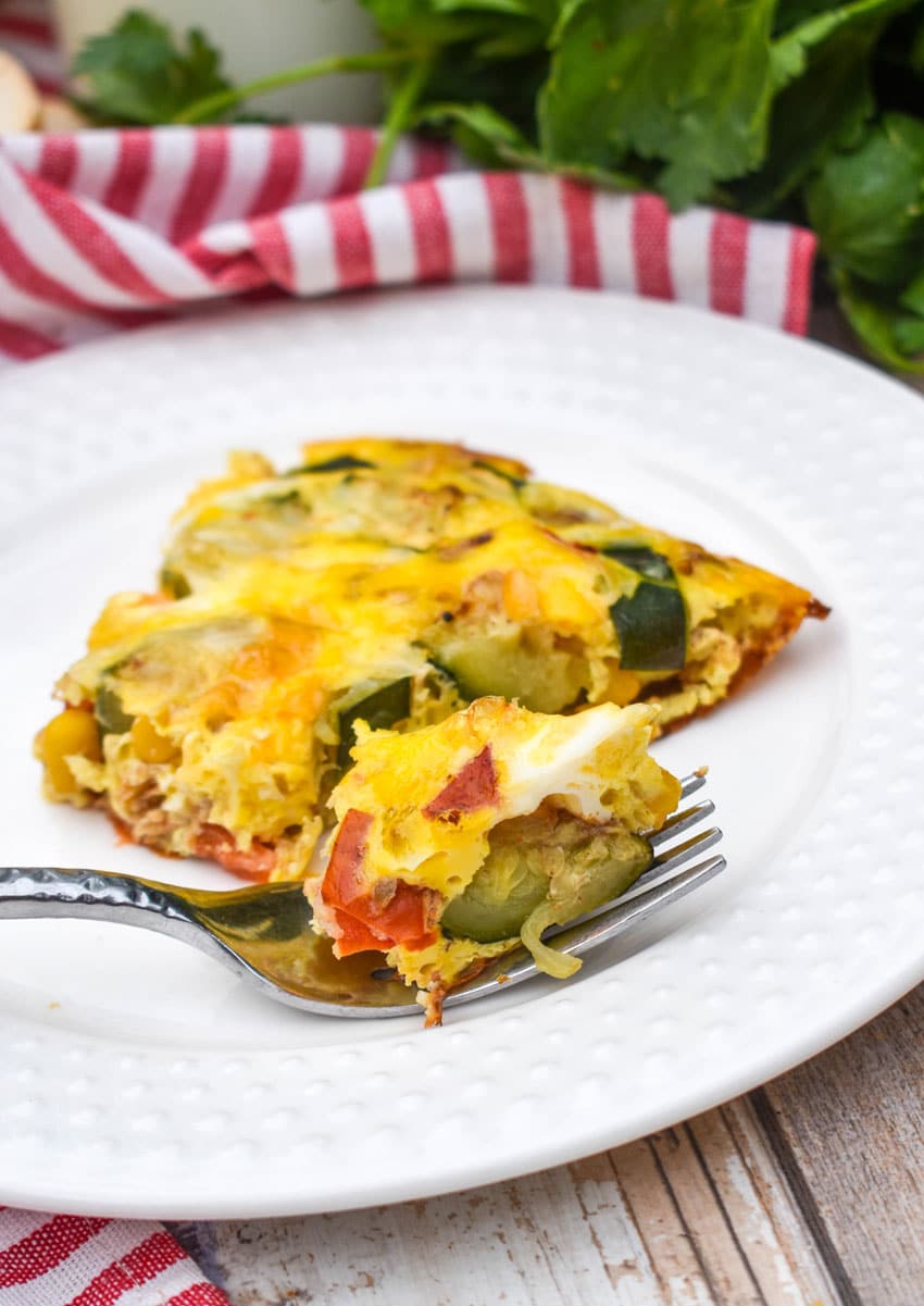 a silver fork resting on a small white plate holding a piece of a garden vegetable fritatta