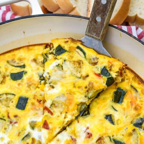 a wood handled spatula lifting a slice of garden vegetable fritatta out of a cast iron skillet