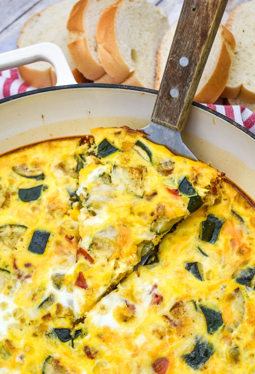 a wood handled spatula lifting a slice of garden vegetable fritatta out of a cast iron skillet