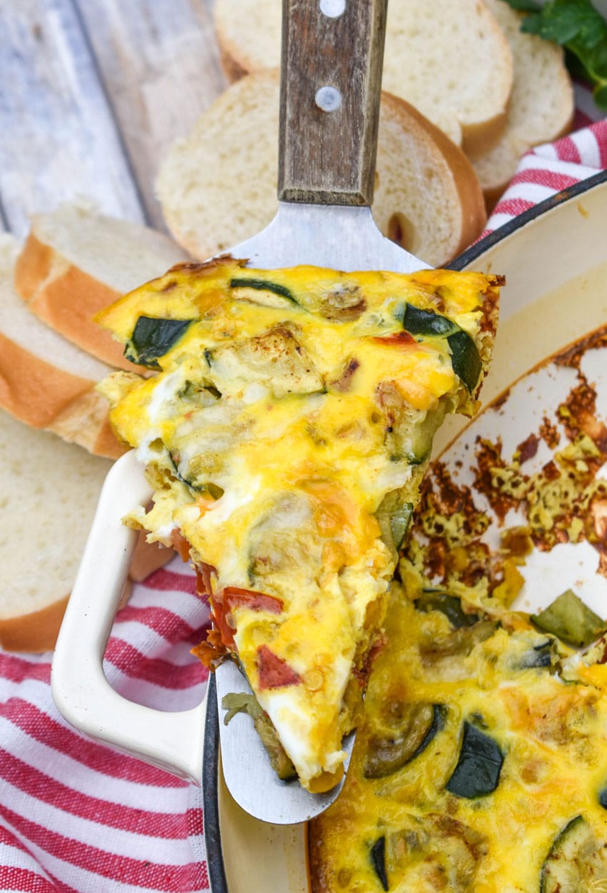 a wood handled spatula lifting a slice of garden vegetable fritatta out of a cast iron skillet