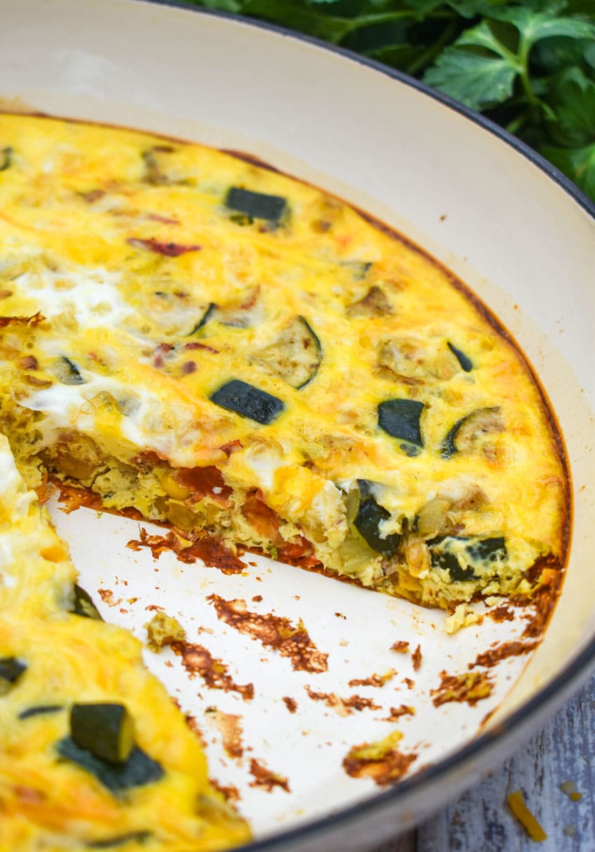 a garden vegetable fritatta in a cast iron skillet with a slice removed to show the filling