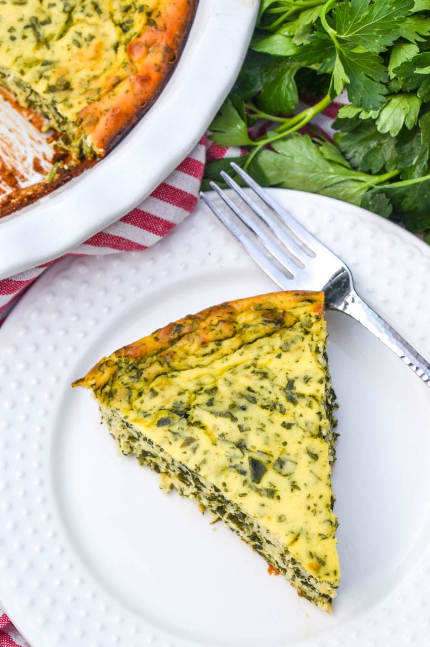 a slice of spinach ricotta pie on a small white plate with a silver fork resting on the side