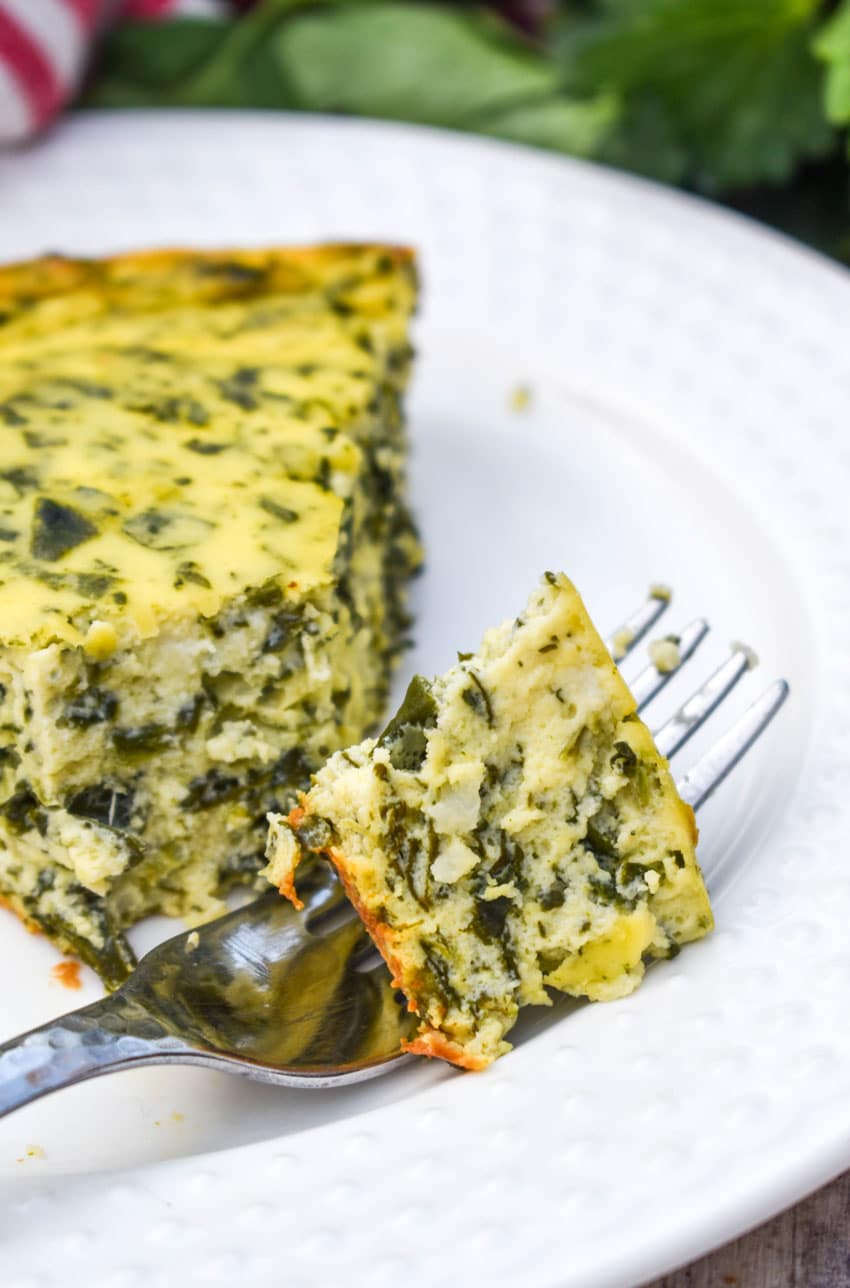 a silver fork holding a piece of spinach ricotta pie resting on the edge of a small white plate