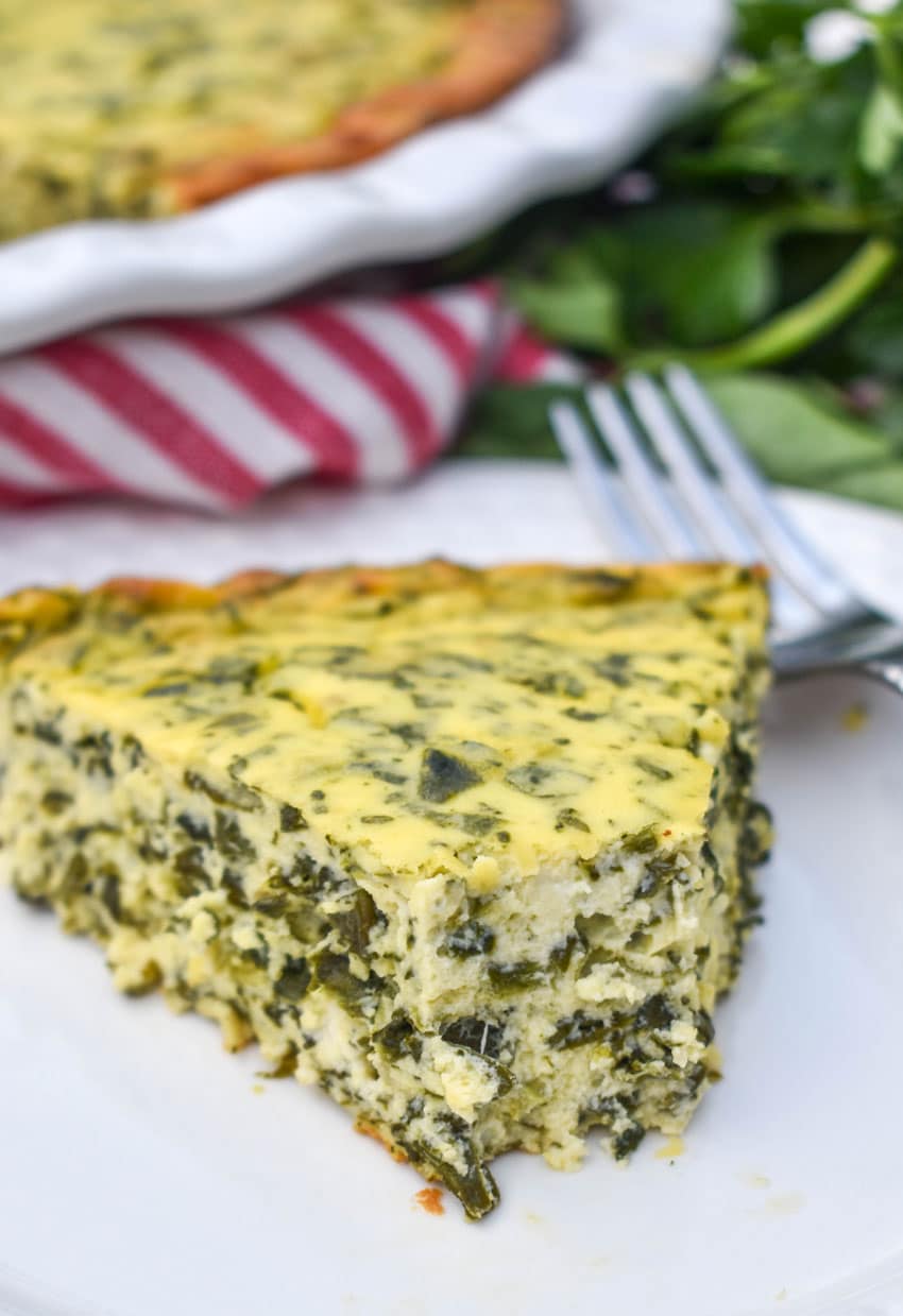 a slice of spinach ricotta pie on a small white plate with a silver fork resting on the side