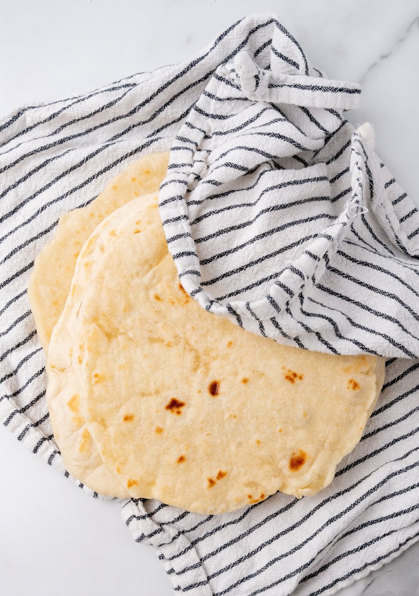 homemade flour tortillas spread out on a cloth napkin on a marble countertop
