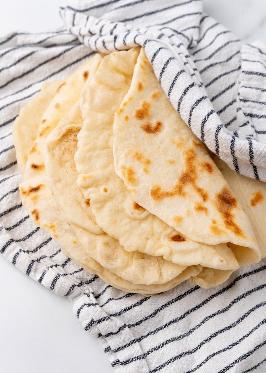 homemade flour tortillas spread out on a cloth napkin on a marble countertop