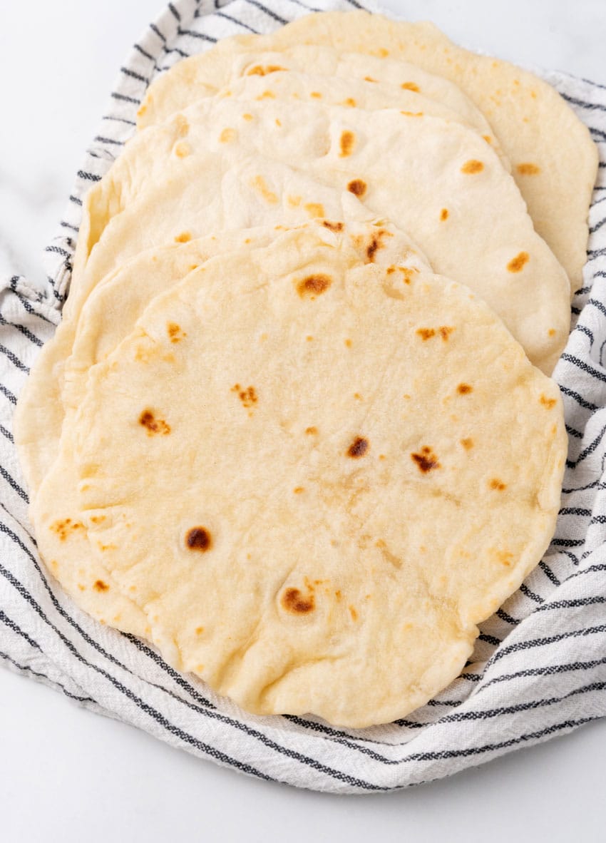 homemade flour tortillas spread out on a cloth napkin on a marble countertop