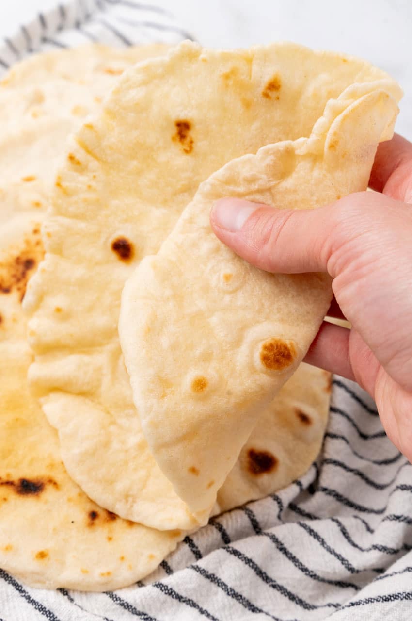 a hand holding up a folded flour tortilla made from scratch