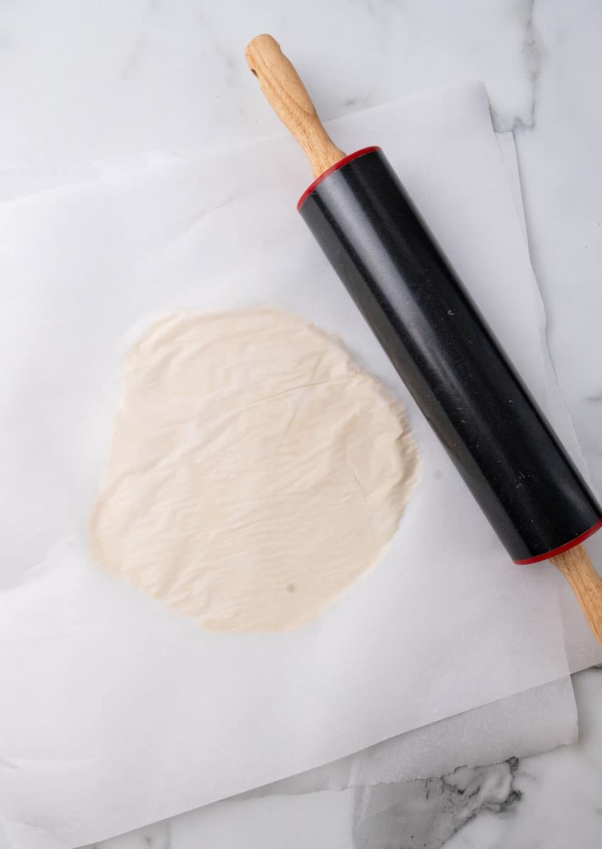 flour tortilla dough rolled flat between two pieces of parchment paper