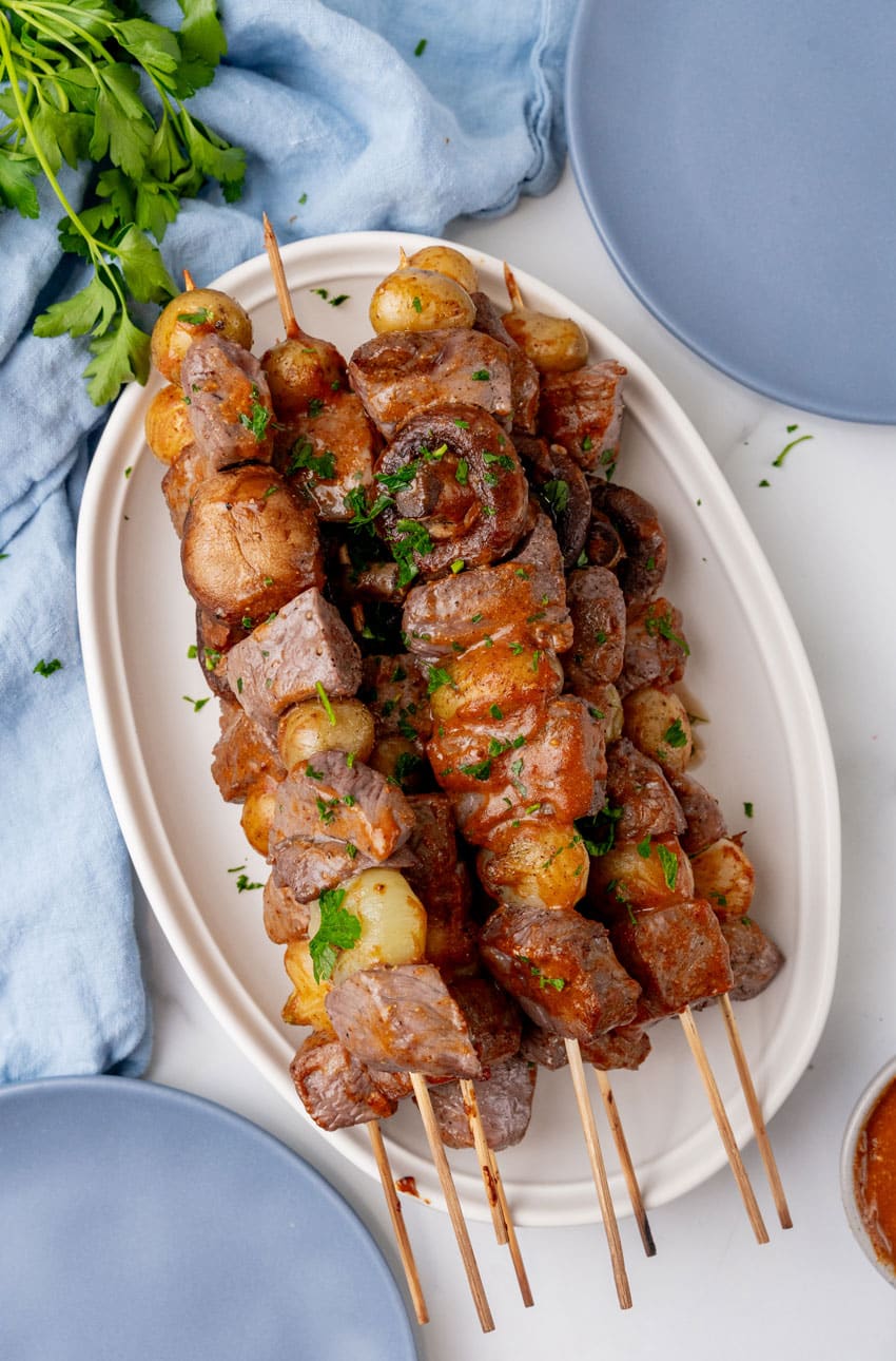 grilled steak kabobs piled on a white serving platter