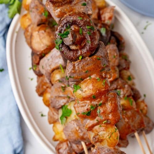 grilled steak kabobs piled on a white serving platter