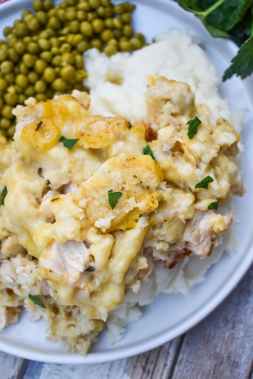 chicken and dumpling casserole next to peas on a white dinner plate