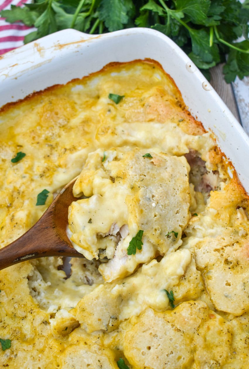 a wooden spoon scooping chicken and dumpling casserole out of a white baking dish