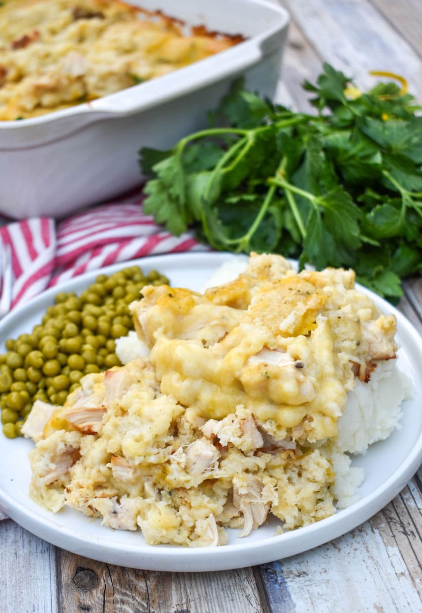 chicken and dumpling casserole next to peas on a white dinner plate