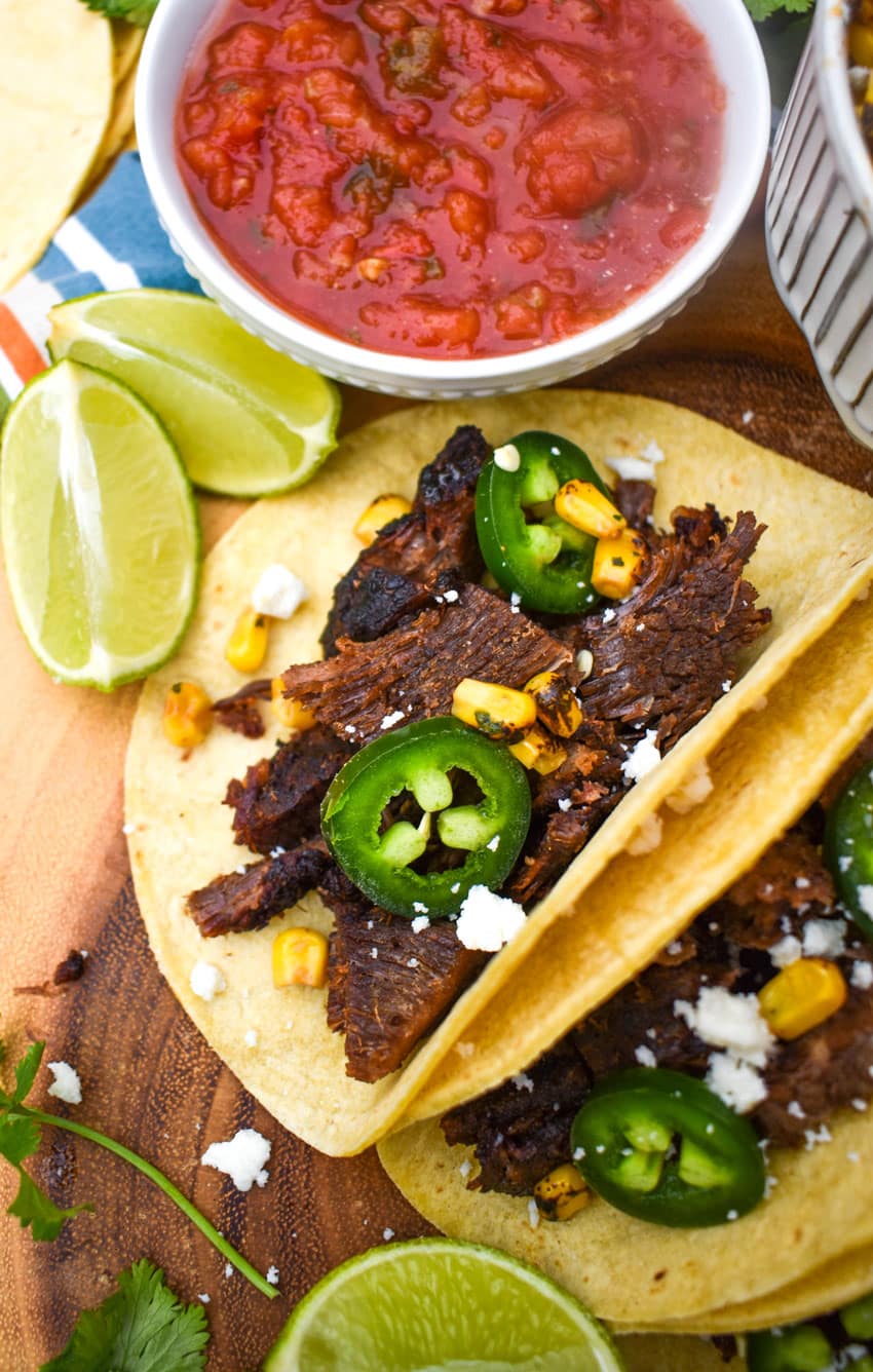 a row of leftover brisket tacos on a wooden cutting board