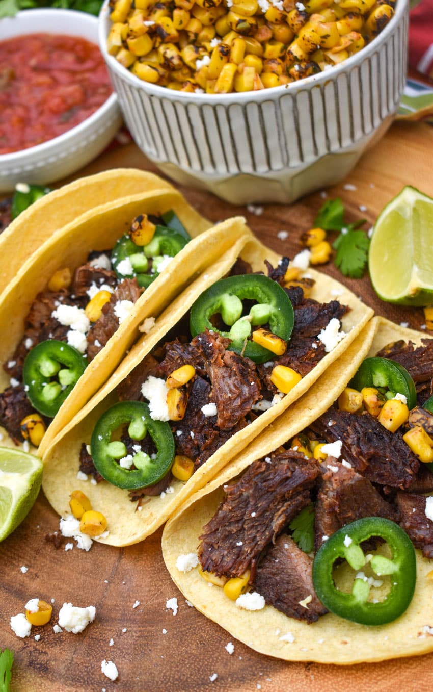 a row of leftover brisket tacos on a wooden cutting board