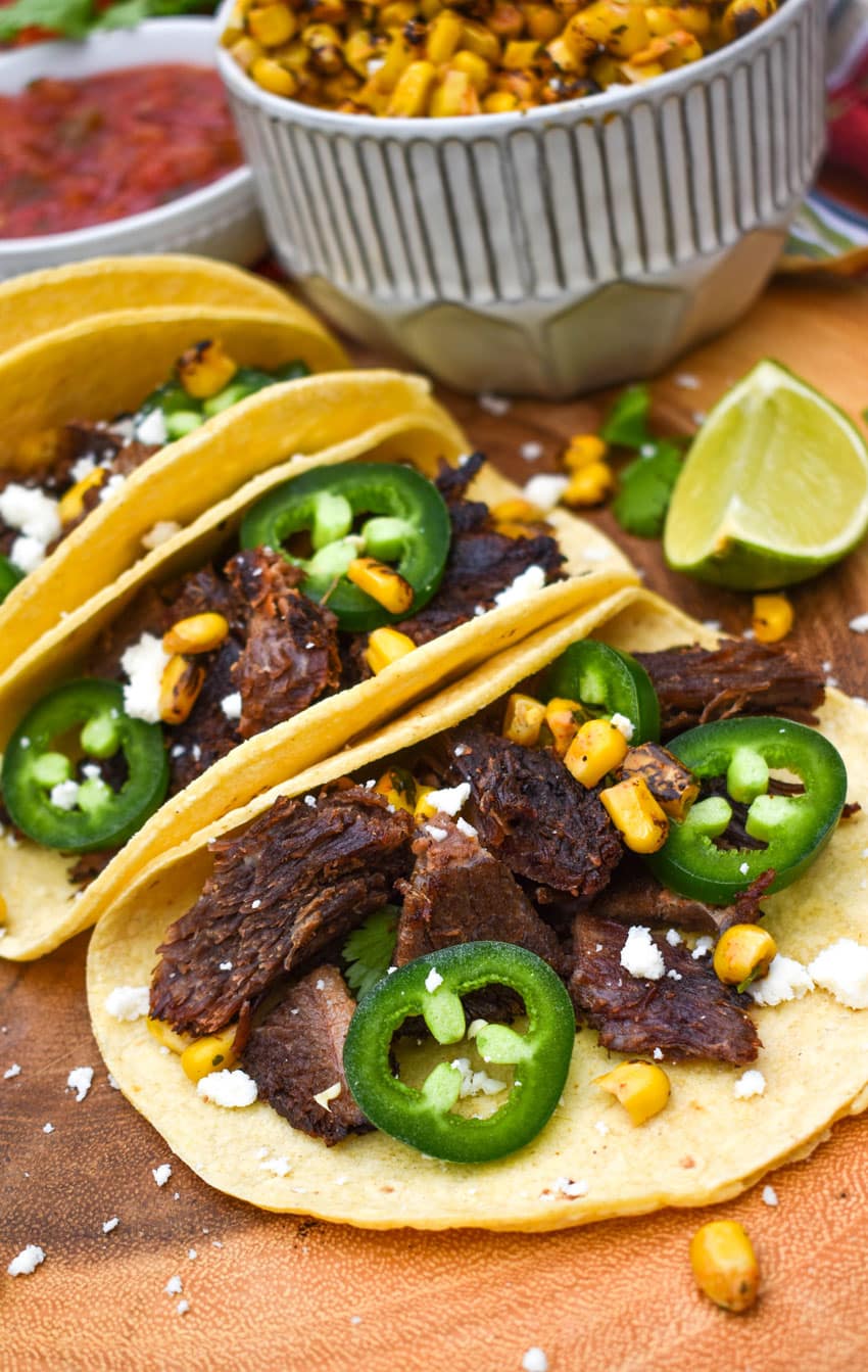 a row of leftover brisket tacos on a wooden cutting board