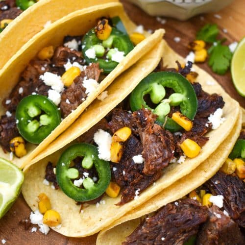 a row of leftover brisket tacos on a wooden cutting board