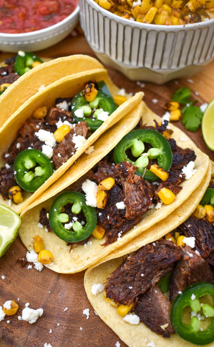 a row of leftover brisket tacos on a wooden cutting board