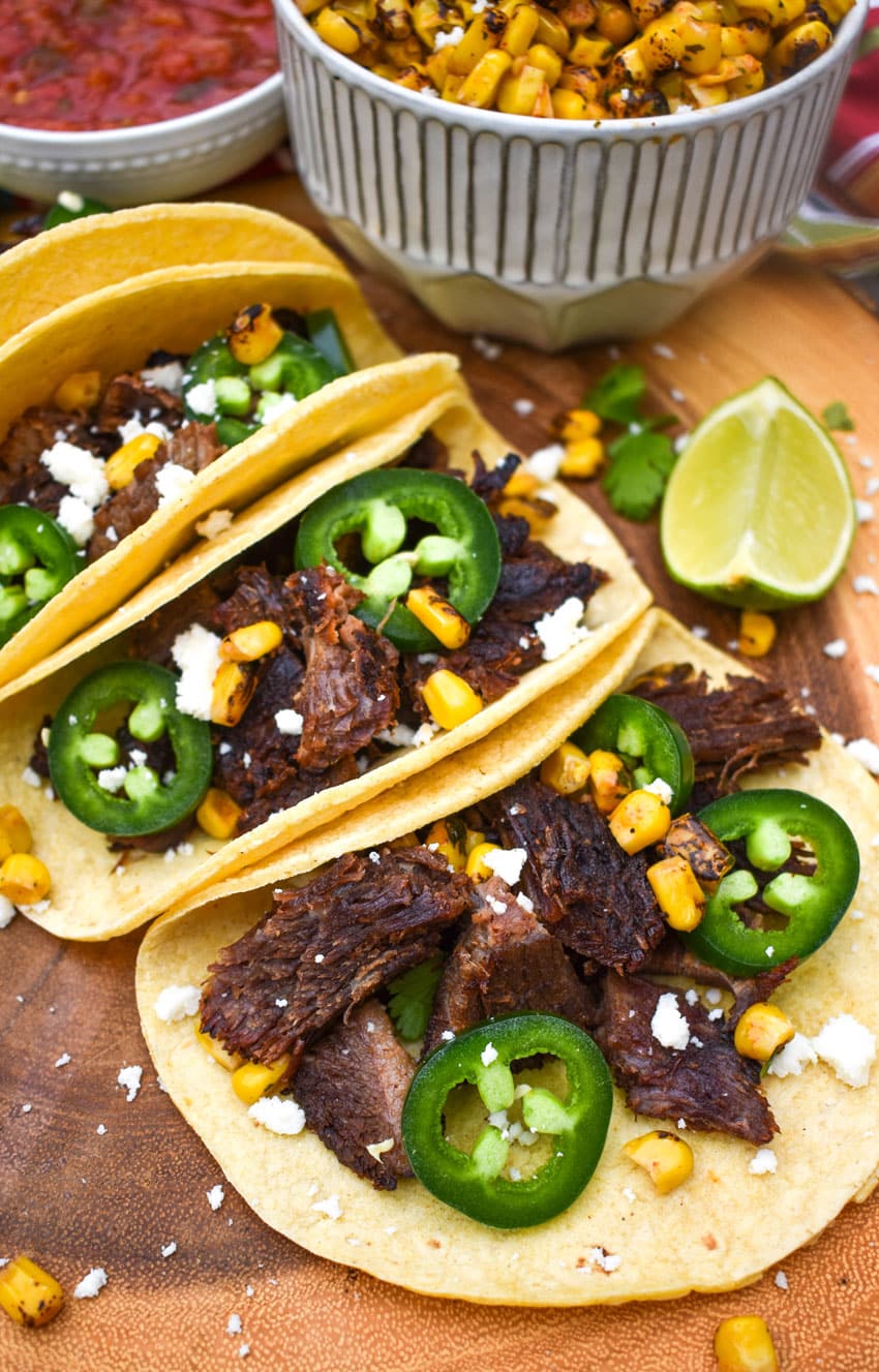 a row of leftover brisket tacos on a wooden cutting board