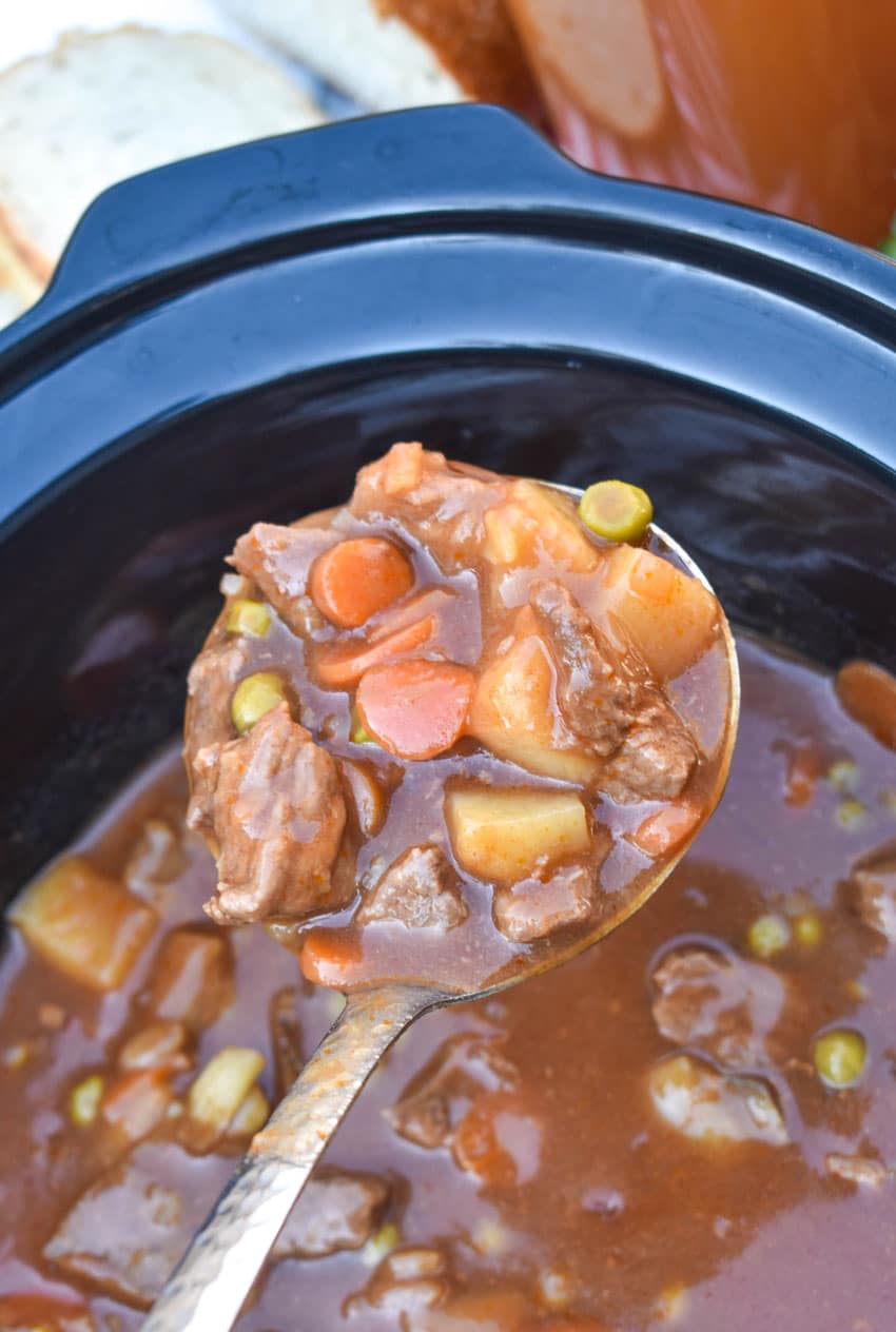 a silver ladle holding up a scoop of apple cider beef stew