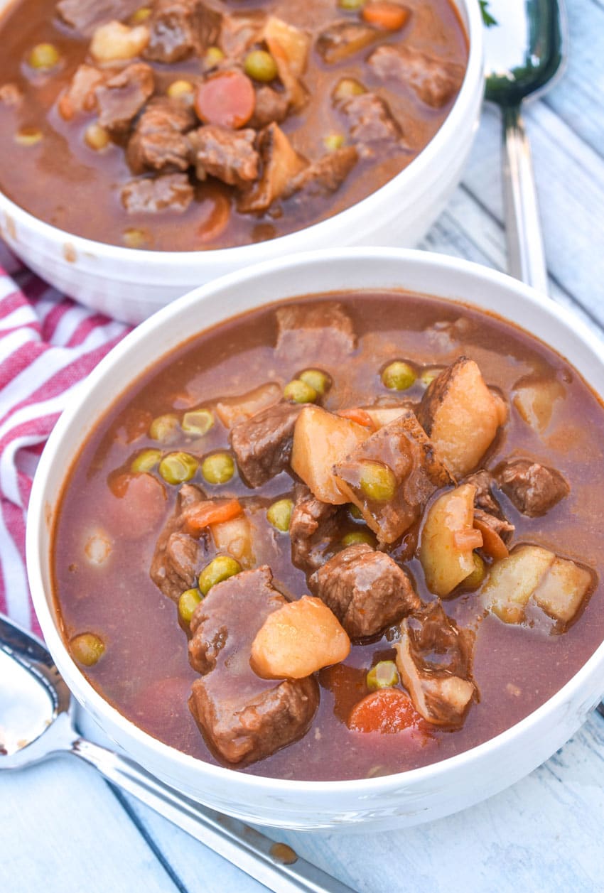 apple cider beef stew in two white bowls on a wooden table