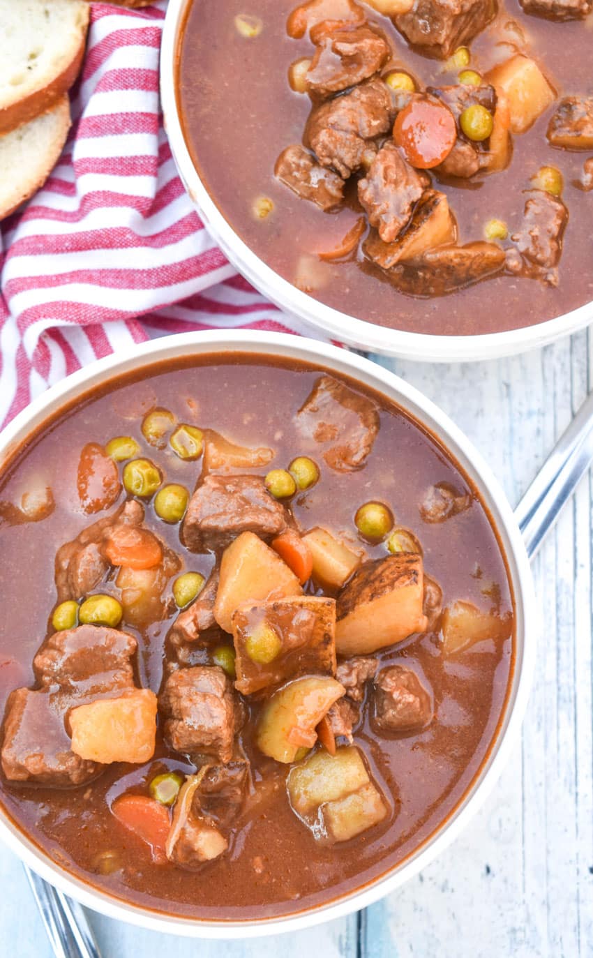 apple cider beef stew in two white bowls on a wooden table