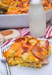 a slice of egg mcmuffin casserole on a small white plate with a glass of milk in the background