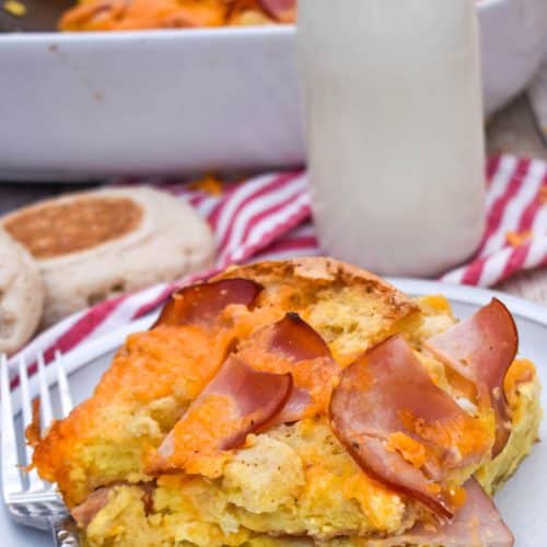 a slice of egg mcmuffin casserole on a small white plate with a glass of milk in the background