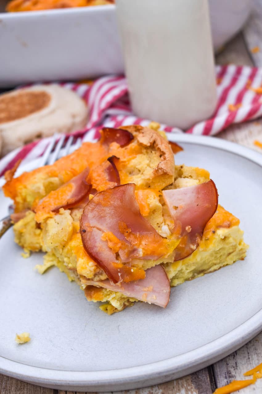 a slice of egg mcmuffin casserole on a small white plate with a glass of milk in the background