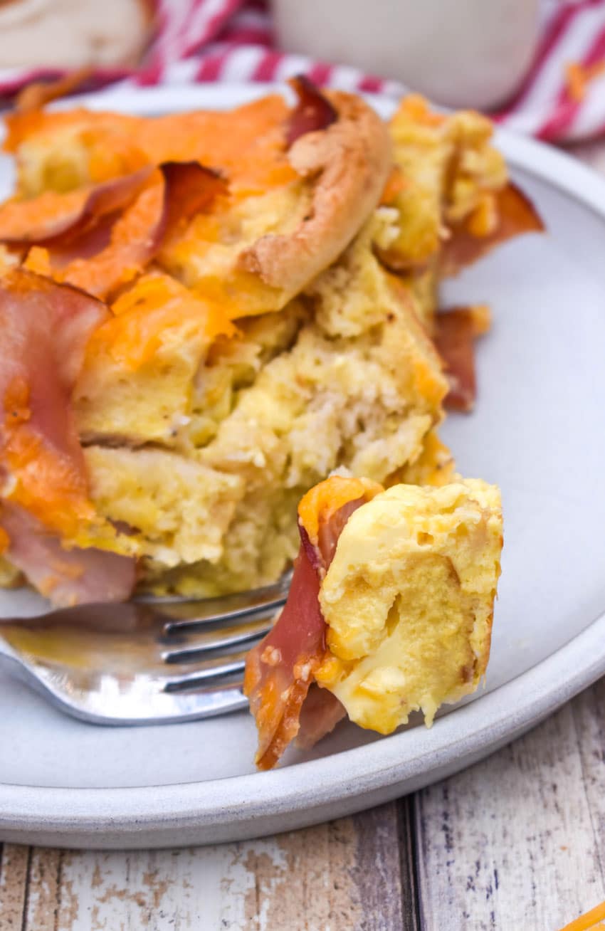 a silver fork holding a piece of egg mcmuffin casserole and resting on the edge of a white plate