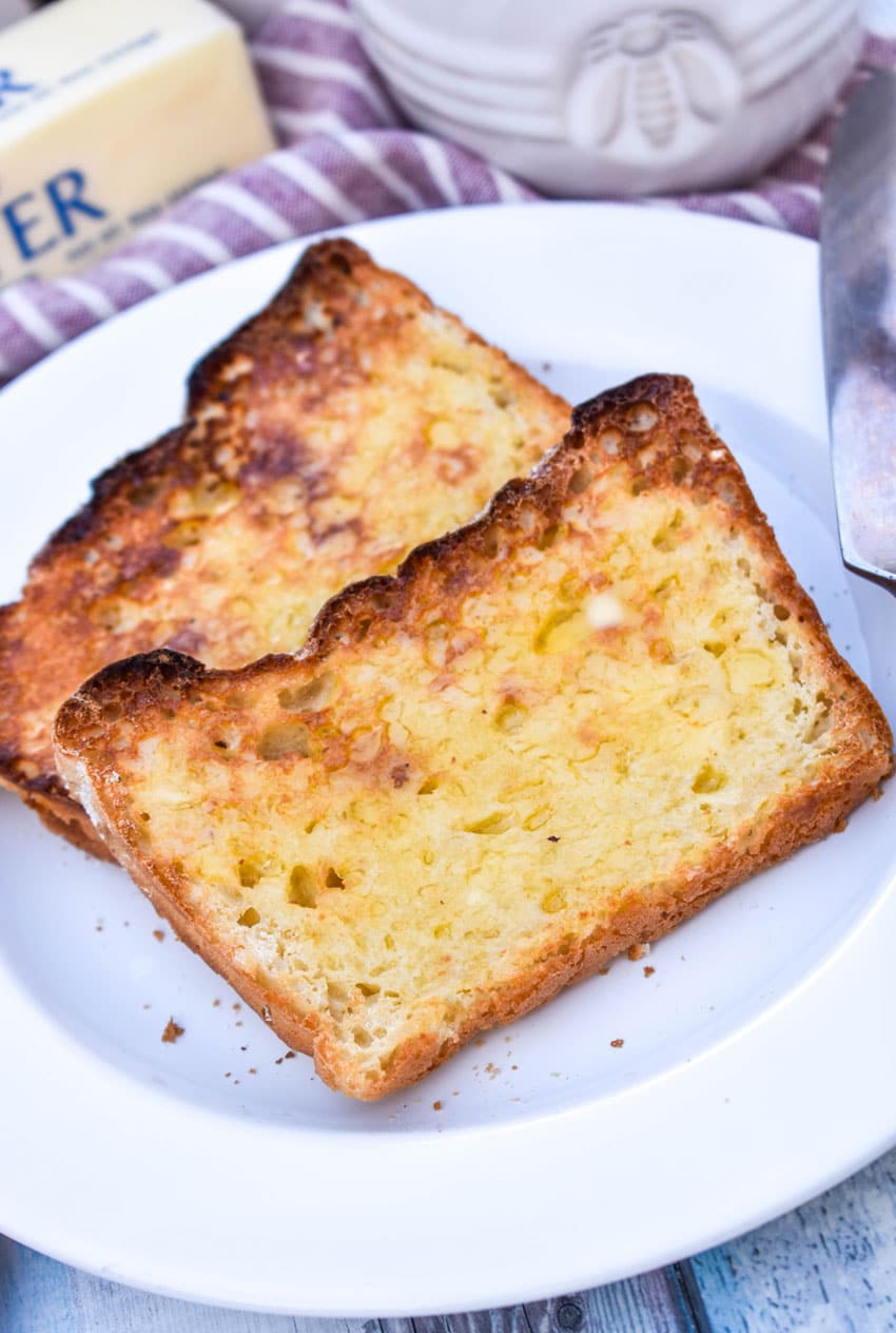two toasted and buttered slices of homemade english muffin bread on a small white plate