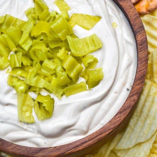 mississippi pot roast dip in a small wooden bowl surrounded by chops and pretzels for dipping