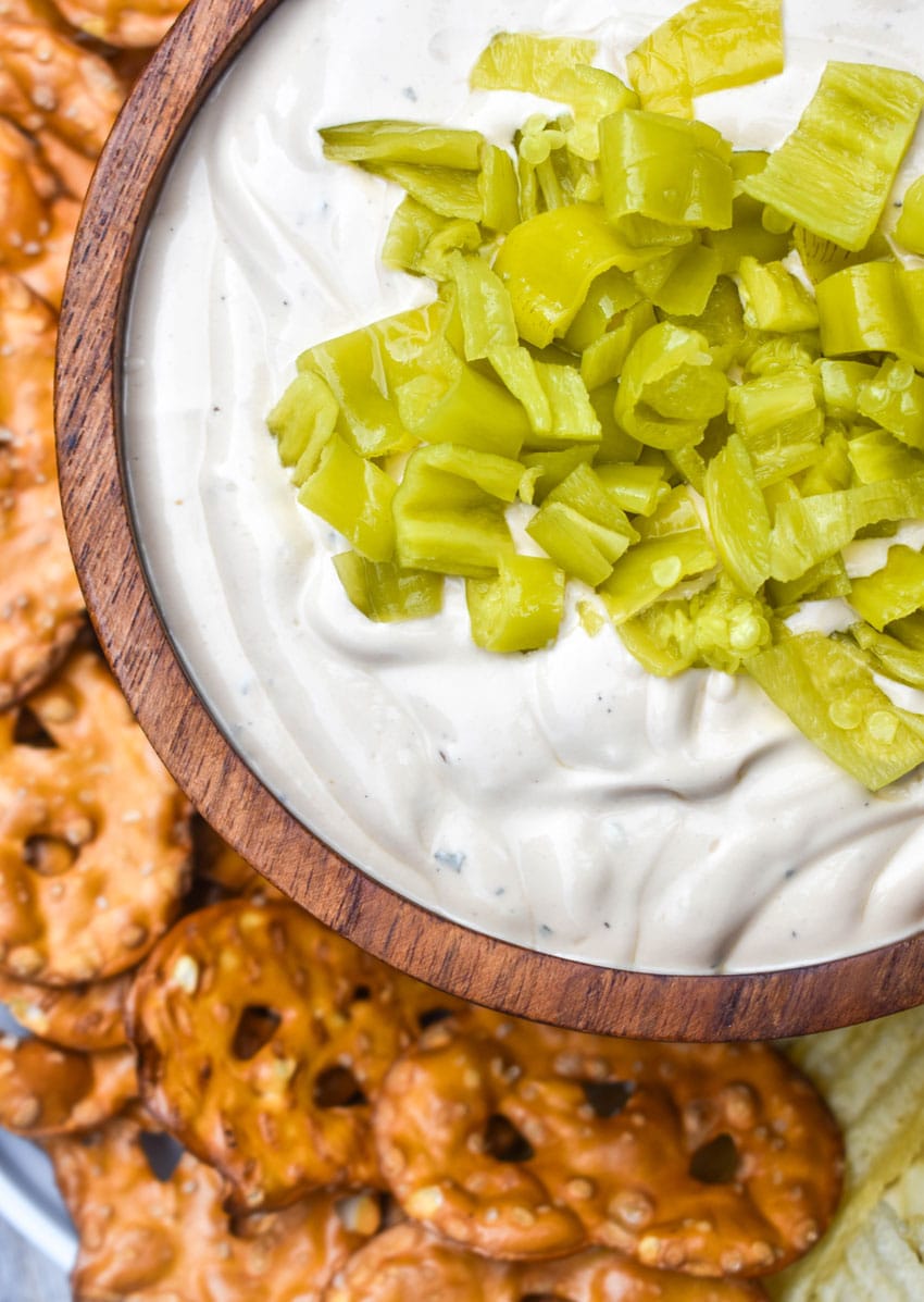 mississippi pot roast dip in a small wooden bowl surrounded by chops and pretzels for dipping
