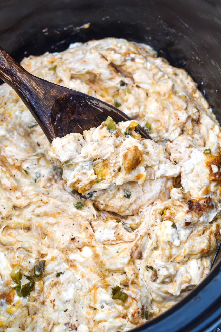 a wooden spoon scooping creamy crab dip out of a black crock
