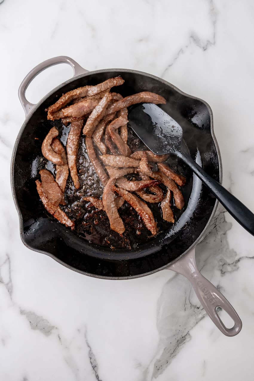 strips of marinated beef in a large cast iron skillet