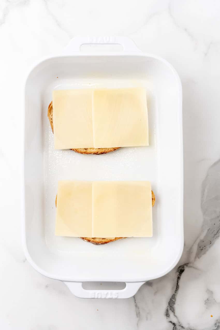 two thick slices of bread topped with slices of swiss cheese in a white baking dish