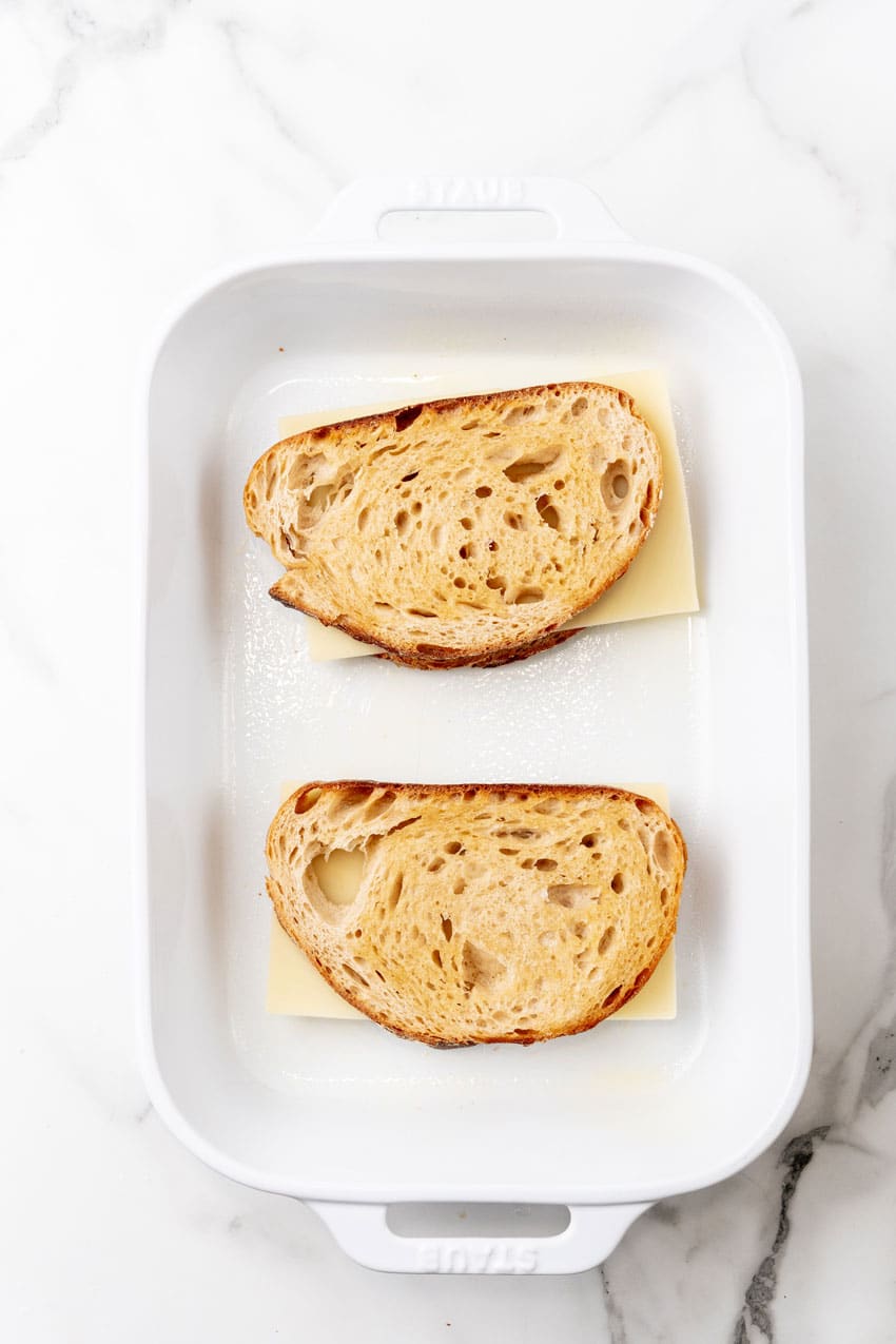 two thick slices of bread topped with slices of swiss cheese in a white baking dish