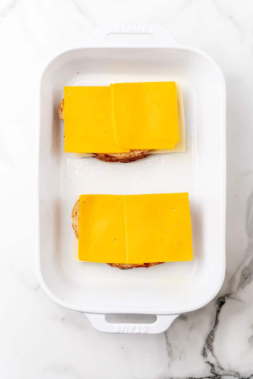 two slices of thick bread topped with cheddar cheese in a white baking dish
