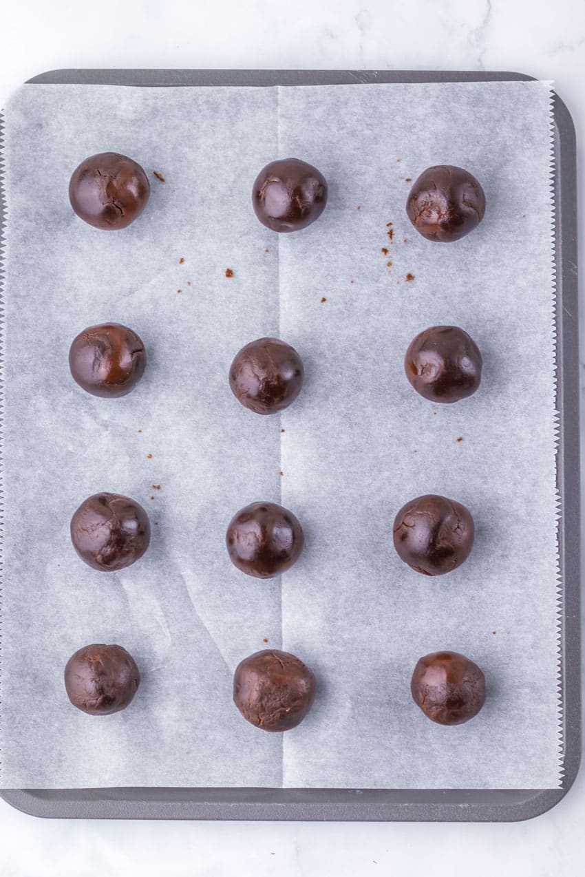 fudgey chocolate brownie balls arranged in rows on a parchment paper lined baking sheet