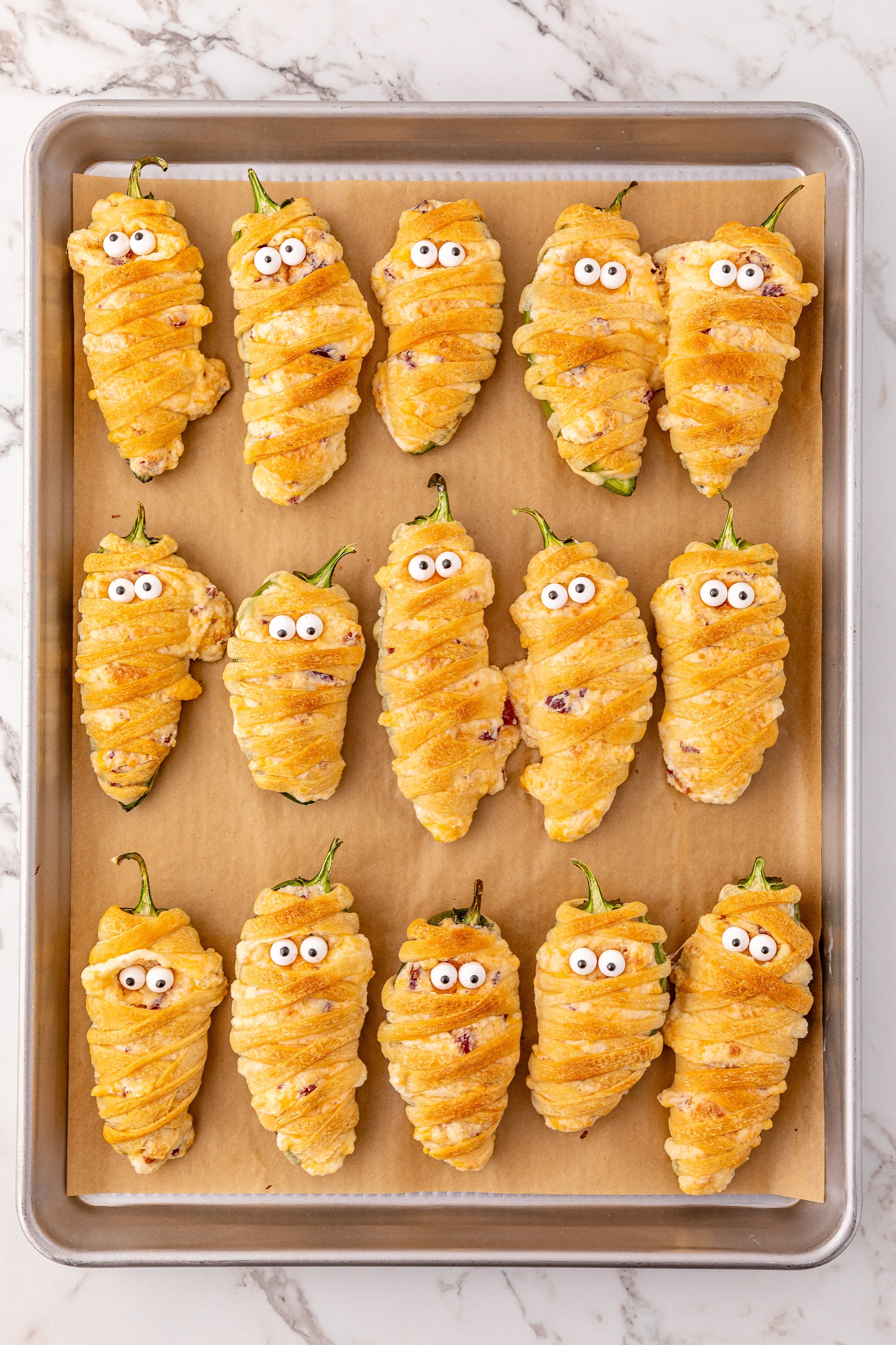 baked jalapeno popper mummies in rows on a parchment lined baking sheet