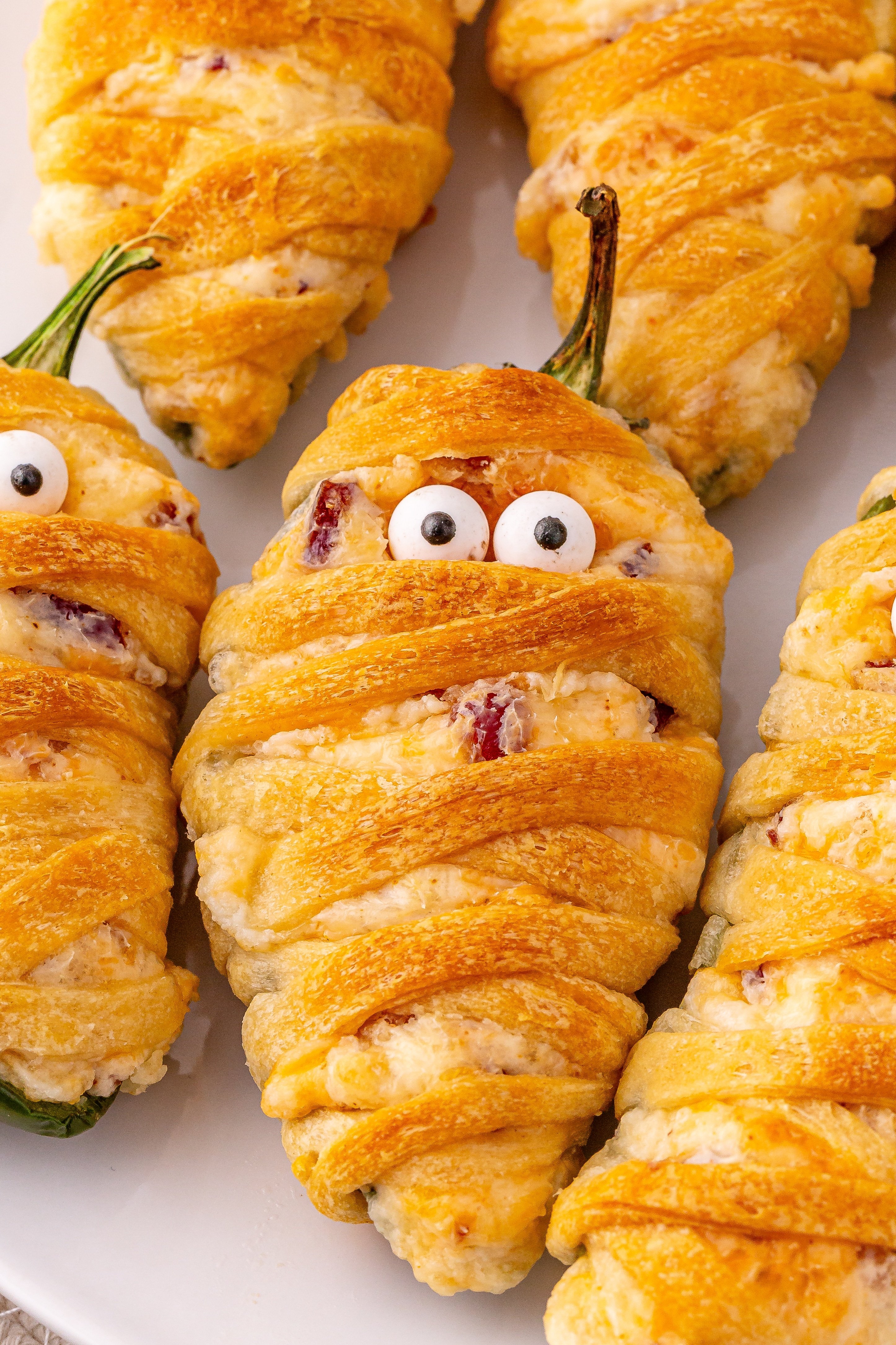 a close up image of jalapeno popper mummies on a white plate