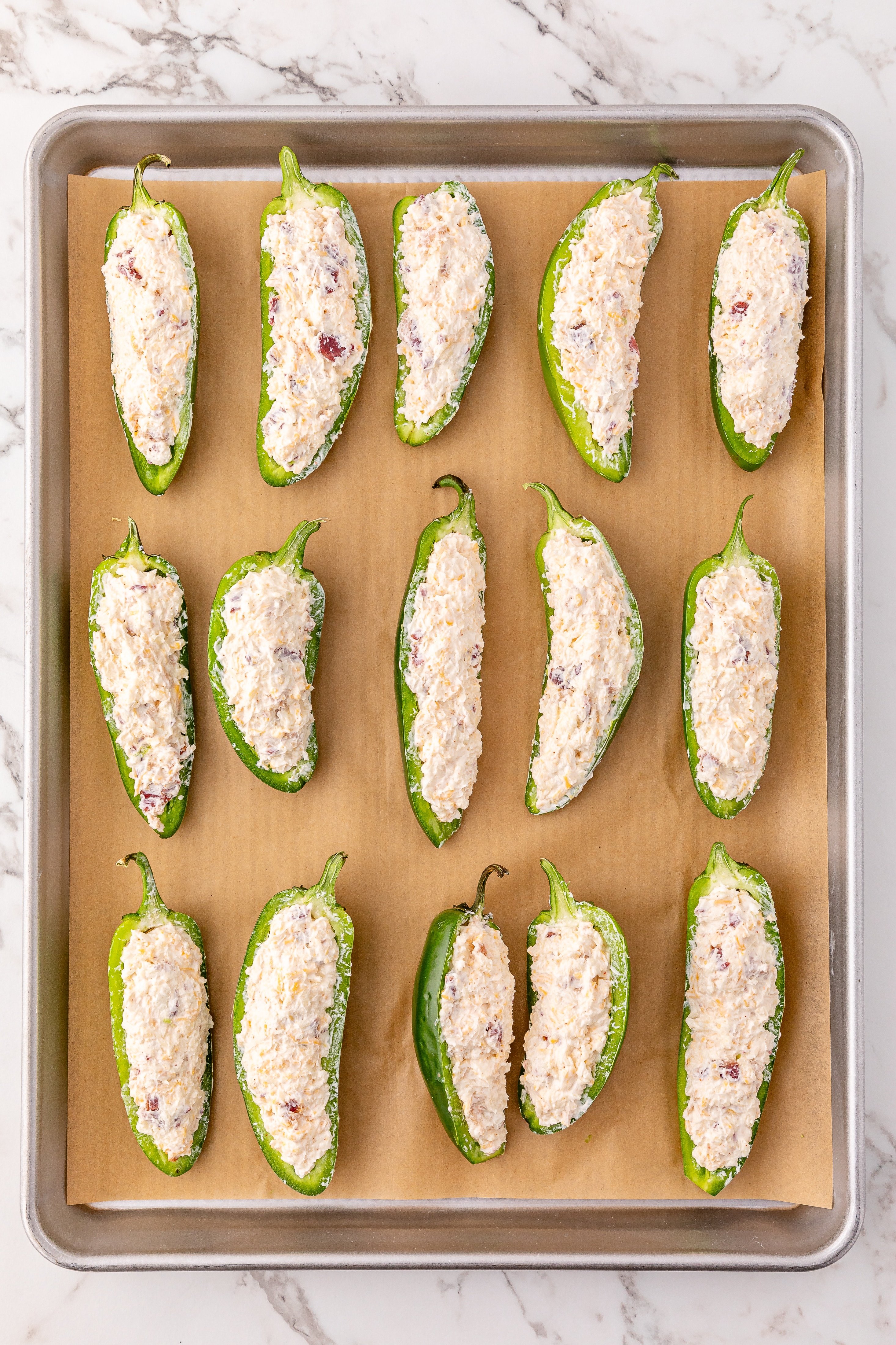 bacon cheddar cream cheese stuffed jalapeno halves on a parchment lined baking sheet