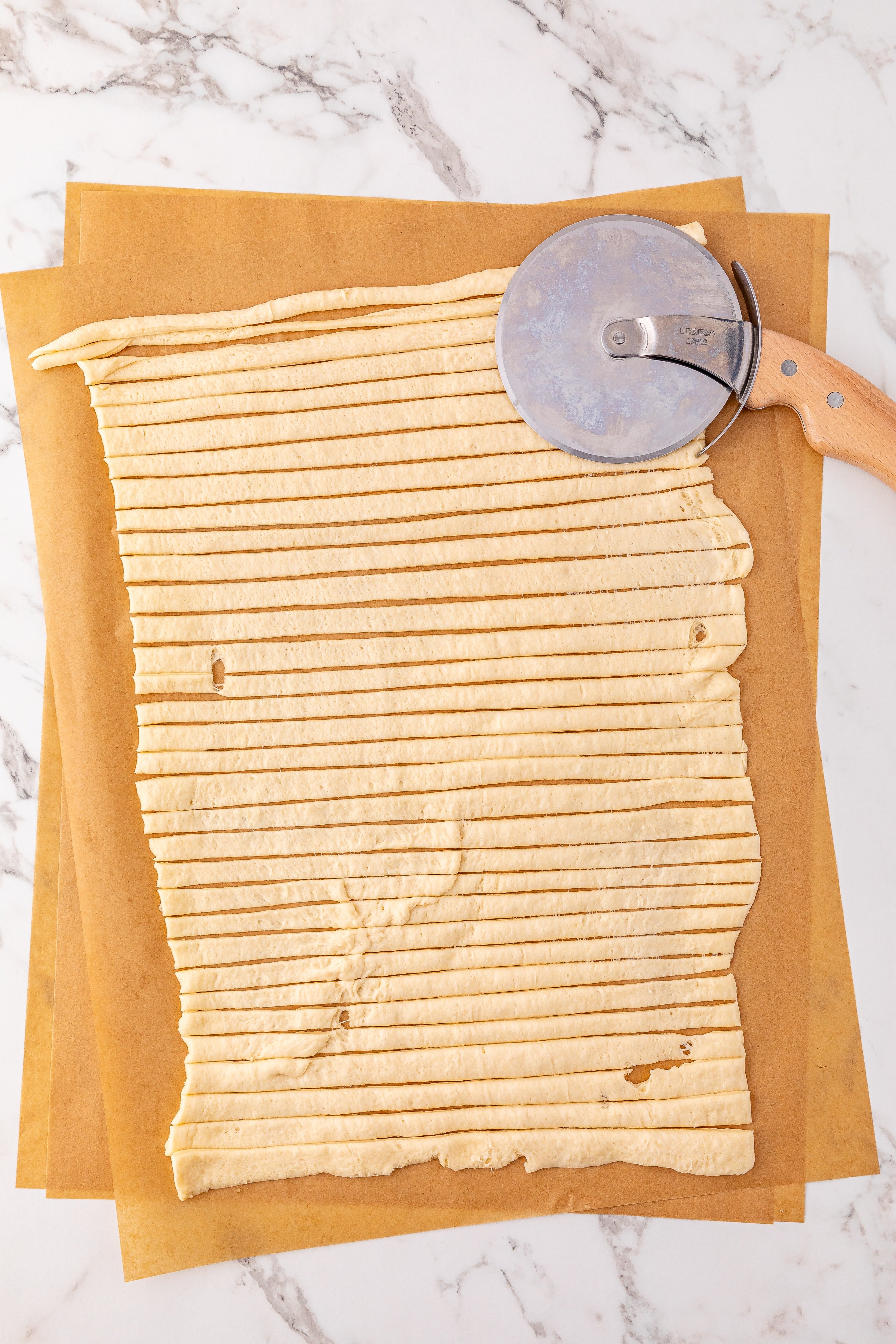 cut strips of a dough on a brown sheet of parchment paper