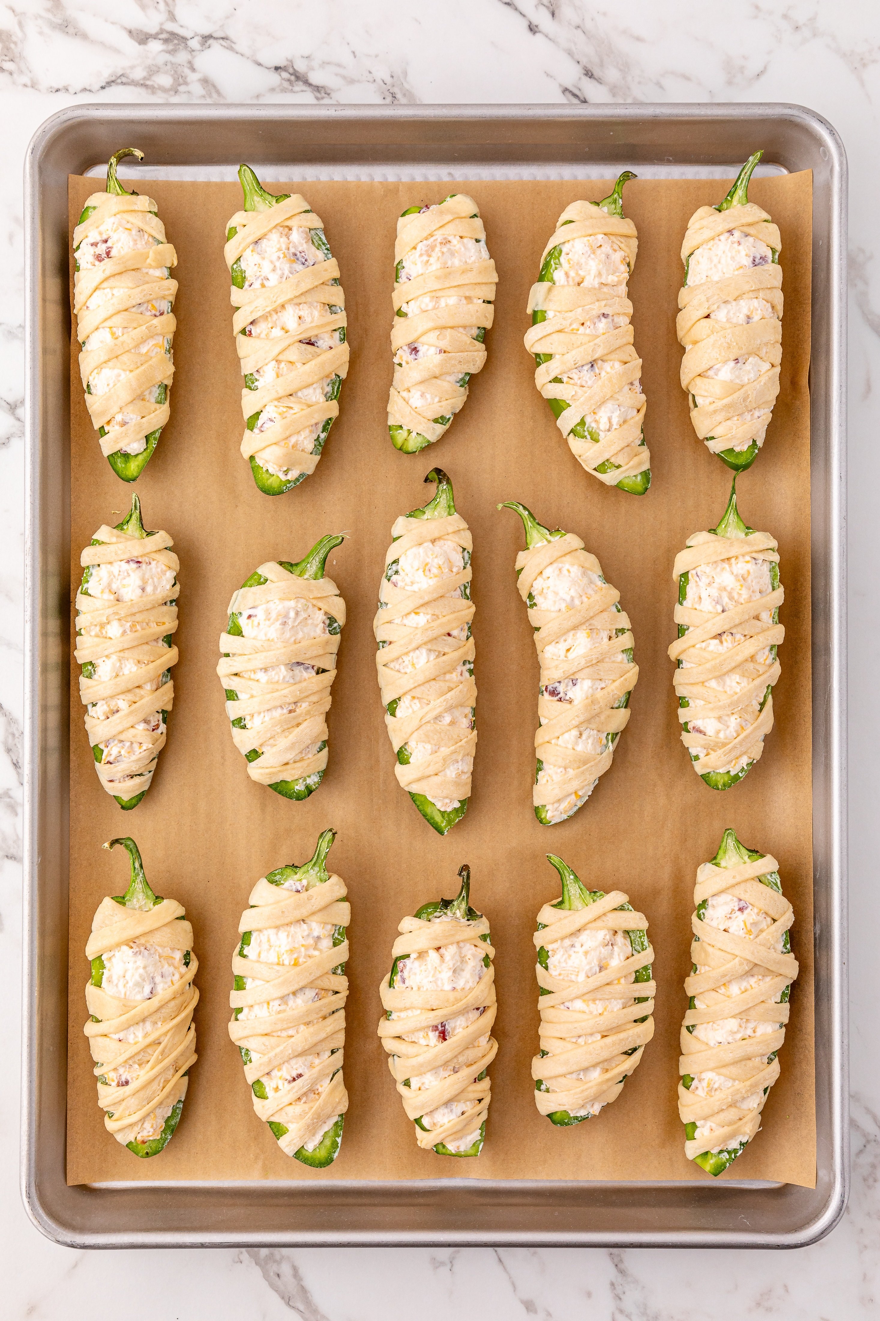 bacon cheddar jalapeno poppers wrapped with pastry day and arranged in rows on parchment paper
